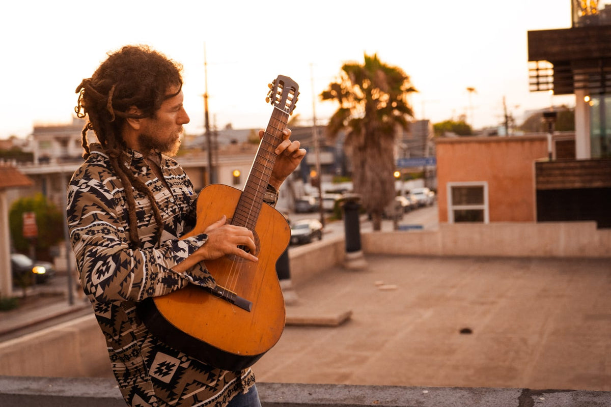Man with dreadlocks playing acoustic guitar on a rooftop at golden hour