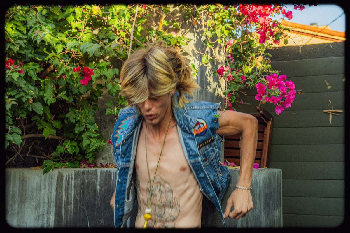 Man in open patched denim vest with bougainvillea in a vintage film-style photo