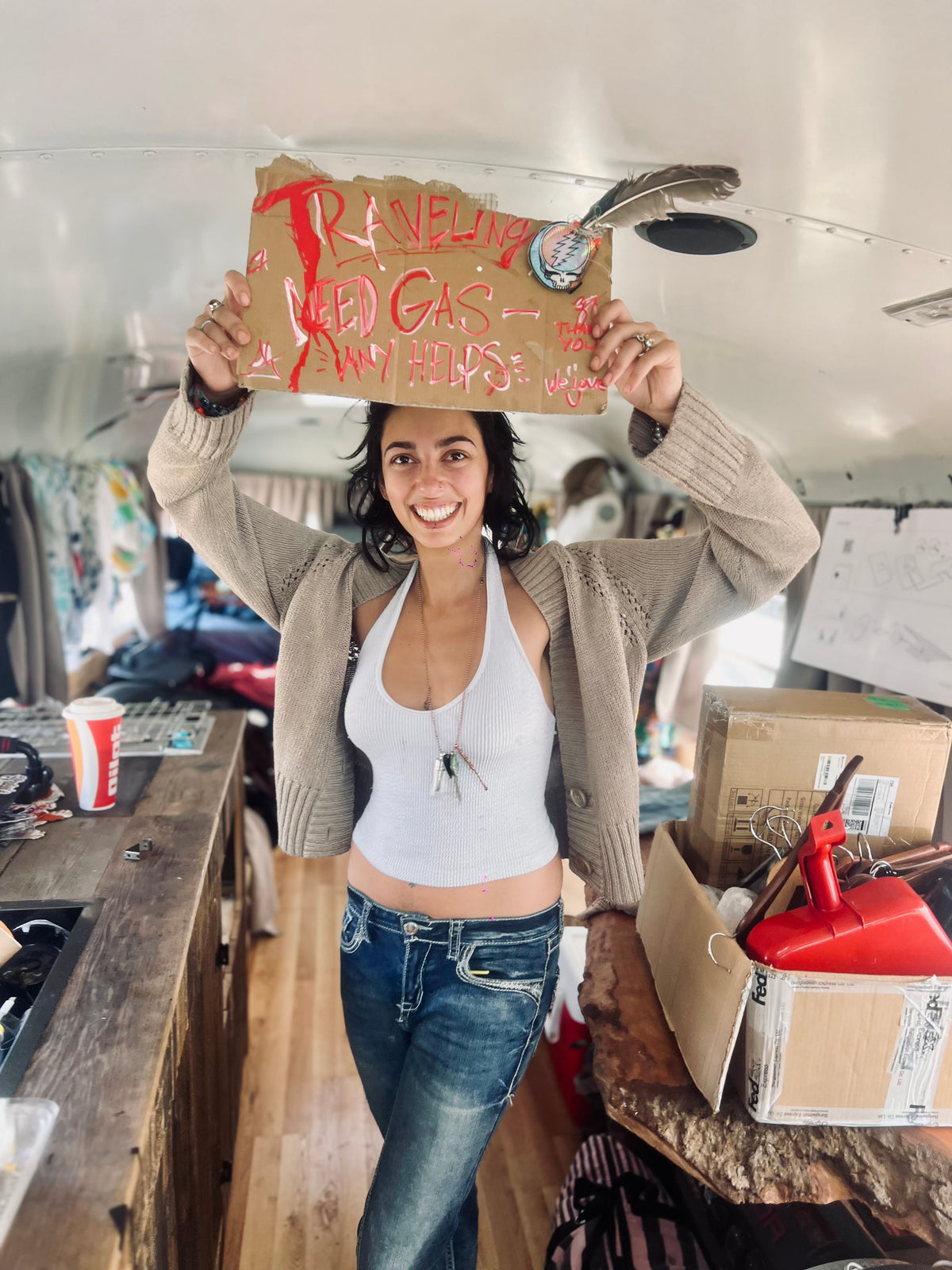 Woman smiling inside the bus holding a handmade Traveling Need Gas cardboard sign