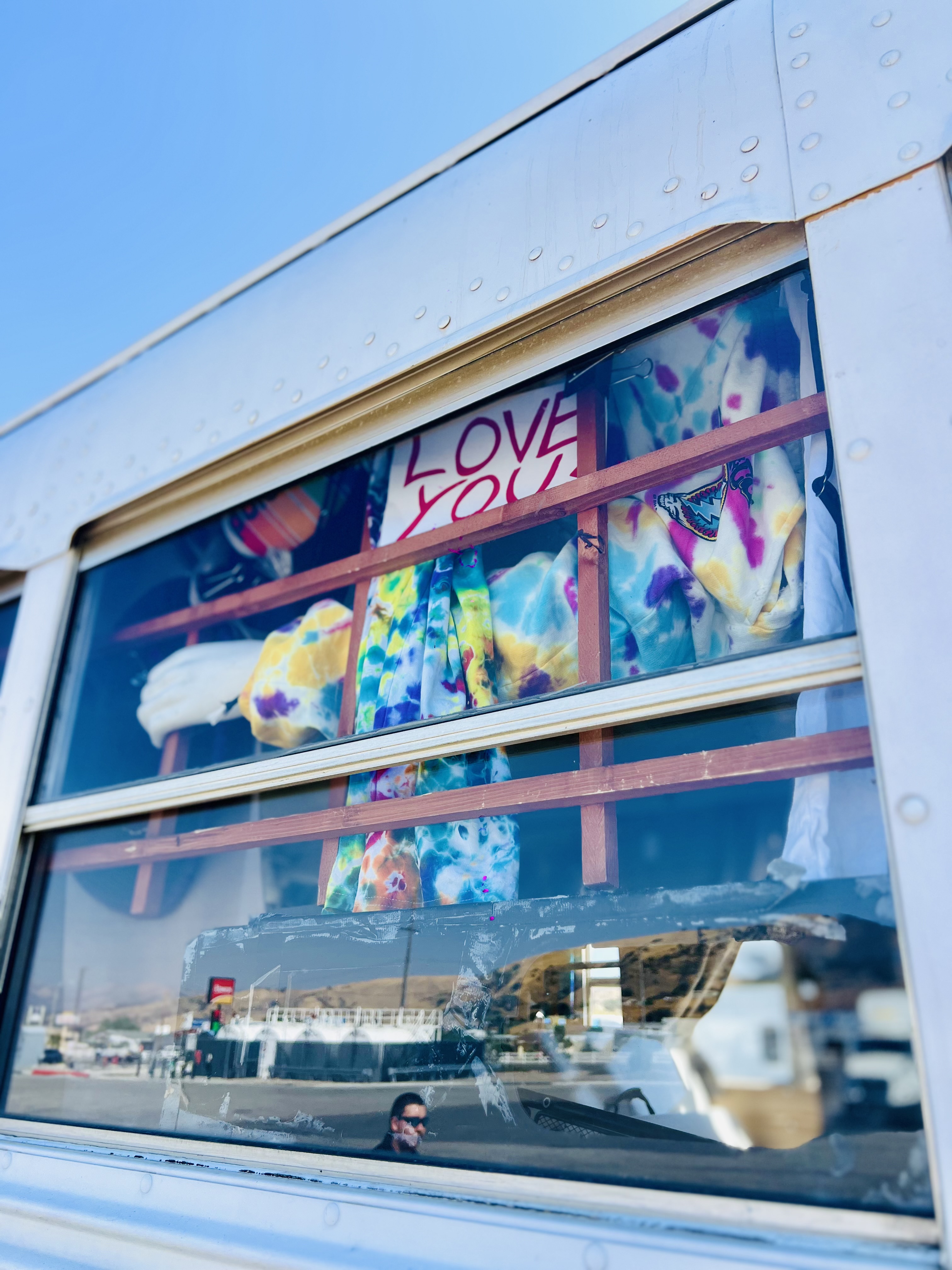 Bus window displaying tie-dye clothing with a Love You sign